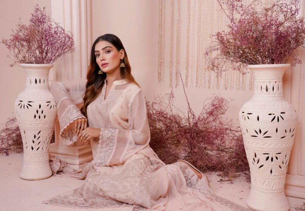 Elegant woman in a beautifully embroidered dress surrounded by decorative vases and dried flowers.