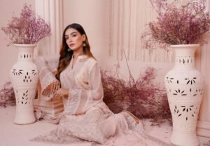 Elegant woman in a beautifully embroidered dress surrounded by decorative vases and dried flowers.